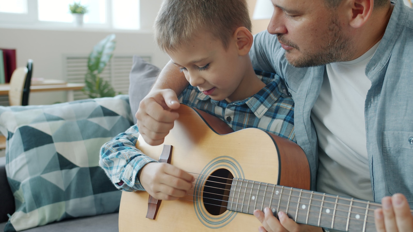 Father teaching son to play guitar at home.