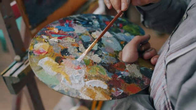 A person holding a wooden palette covered in colorful oil paints and a brush